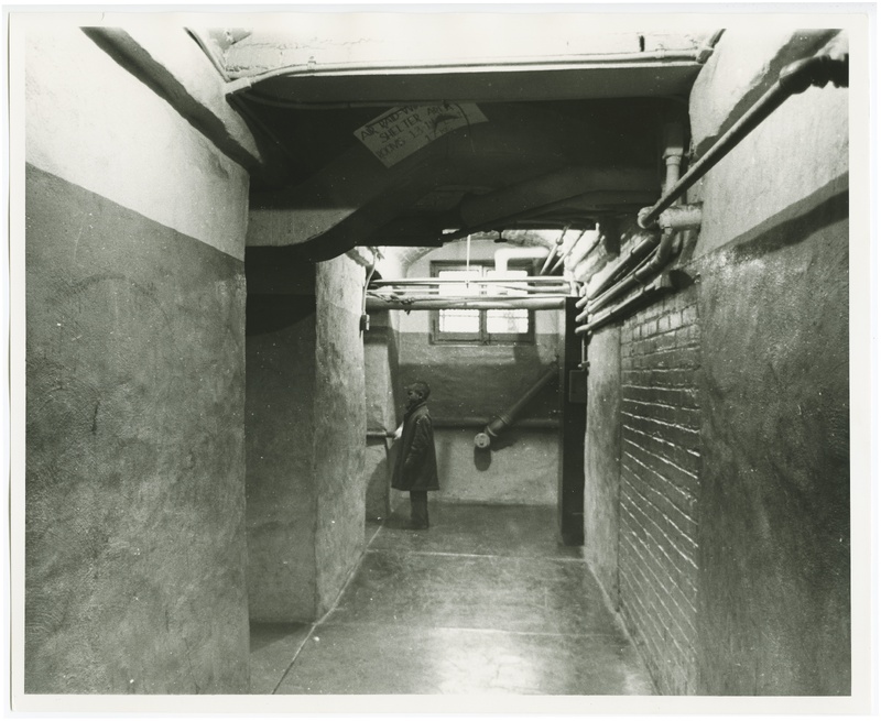 Historic image of a child standing in a basement hallway at a school.