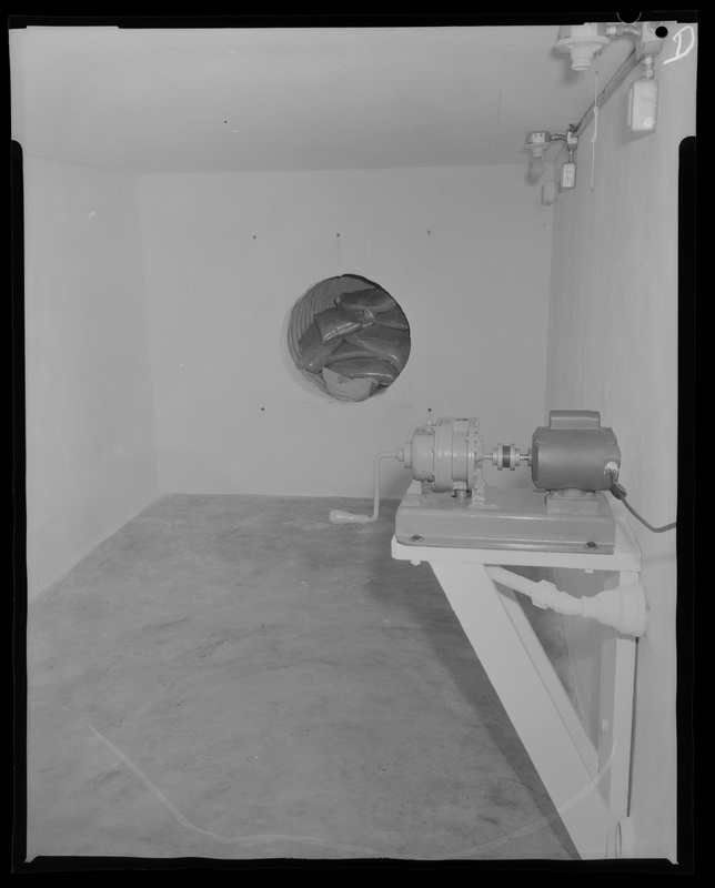 Historic image of the inside of a concrete bomb shelter with storage nook and hand-crank device.