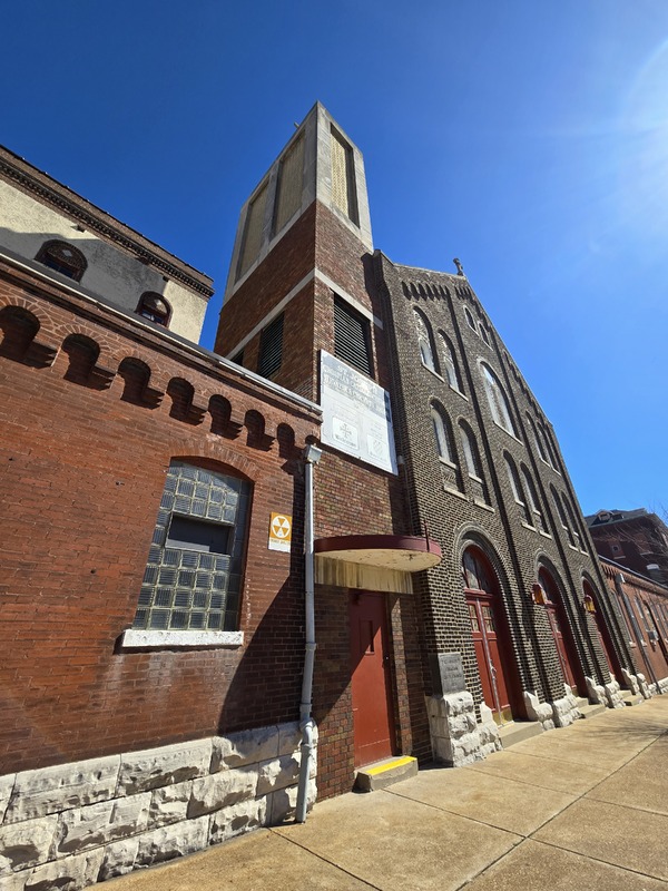 Front view of St. Joseph church building with fallout shelter sign near an entryway.