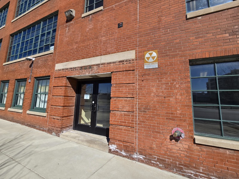 View of KIPP School building side entryway with fallout shelter sign next to it.
