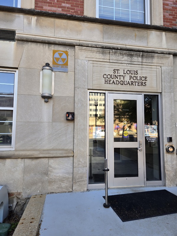 Close up view of doorway to County Police building with fallout shelter sign next to it.