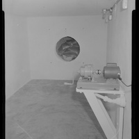 Historic image of the inside of a concrete bomb shelter with storage nook and hand-crank device.