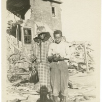 WOMAN AND BOY IN FRONT OF TORNADO DAMAGED HOME